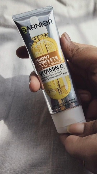 A high-contrast, hand-held product demonstration of a Vitamin C serum cleanser set against a neutral background.